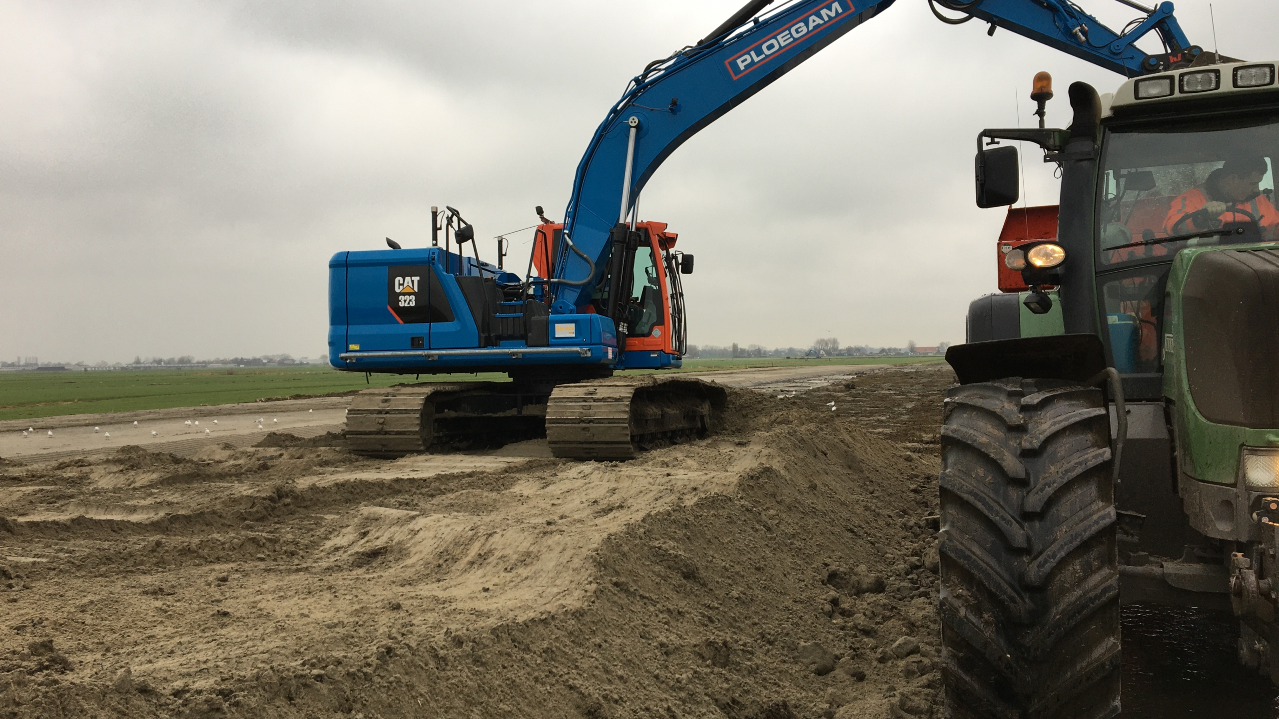 Ploegam rupskraan op het zand schept zand in de bak van een tractor
