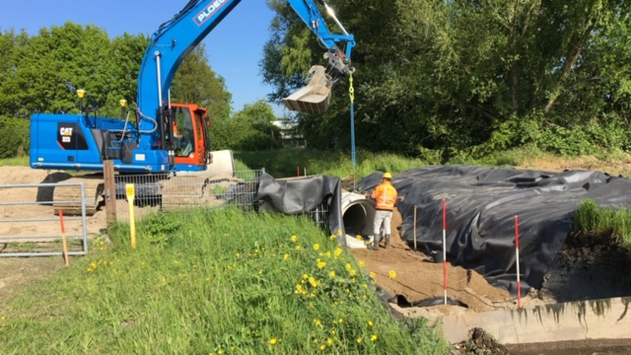 Blauwe kraan en man met veiligheidsjas en helm aan het werk op bouwplaats
