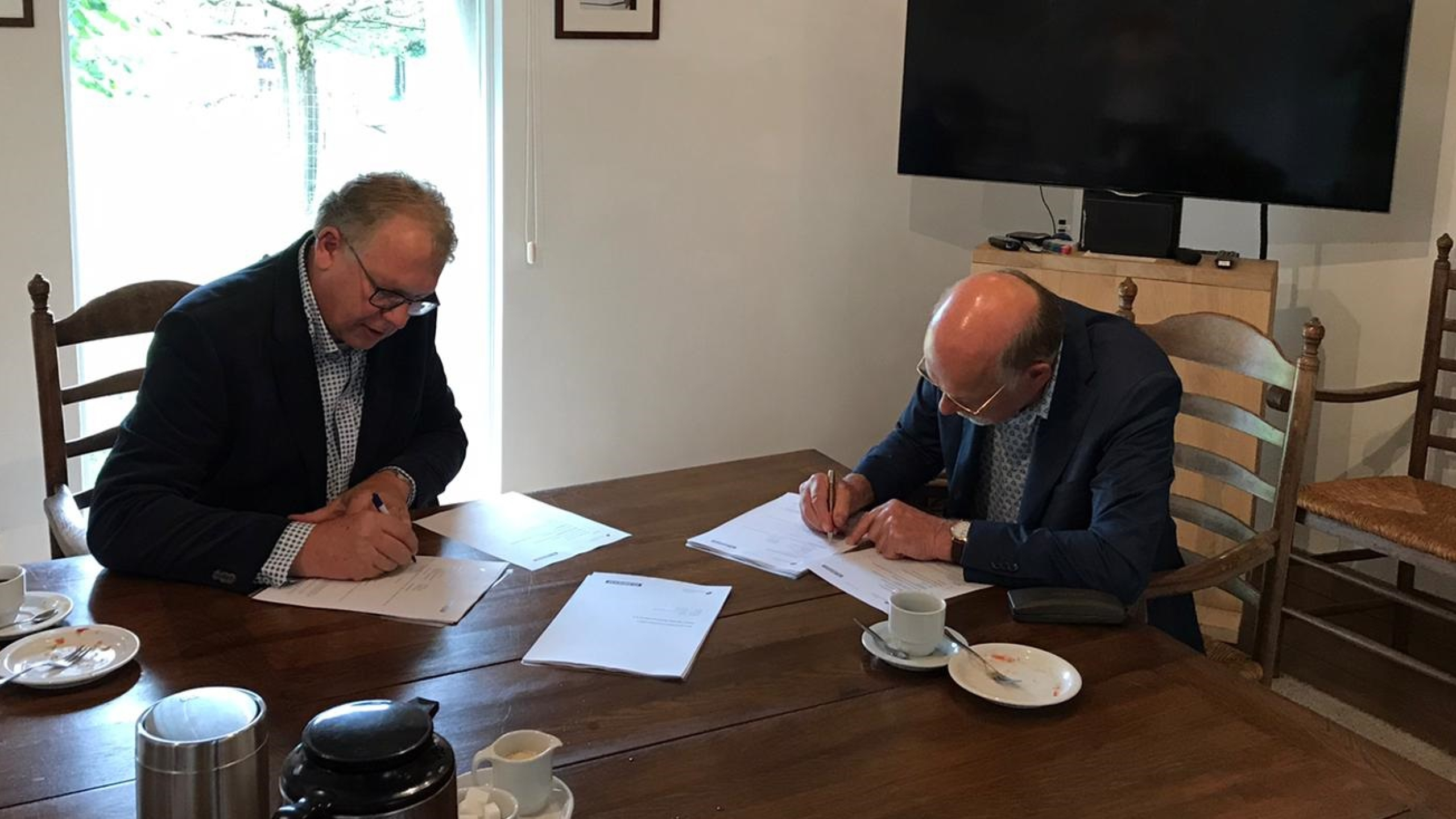 Twee mannen in pak tekenen documenten aan een houten tafel