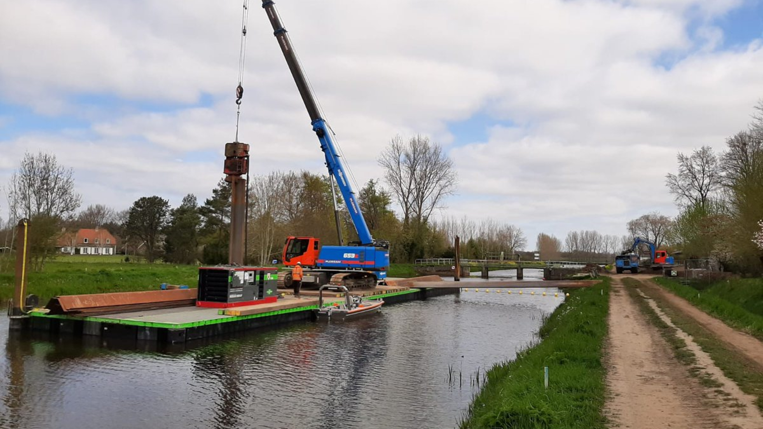 Blauwe Ploegam kraan plaatst damwanden vanaf een ponton