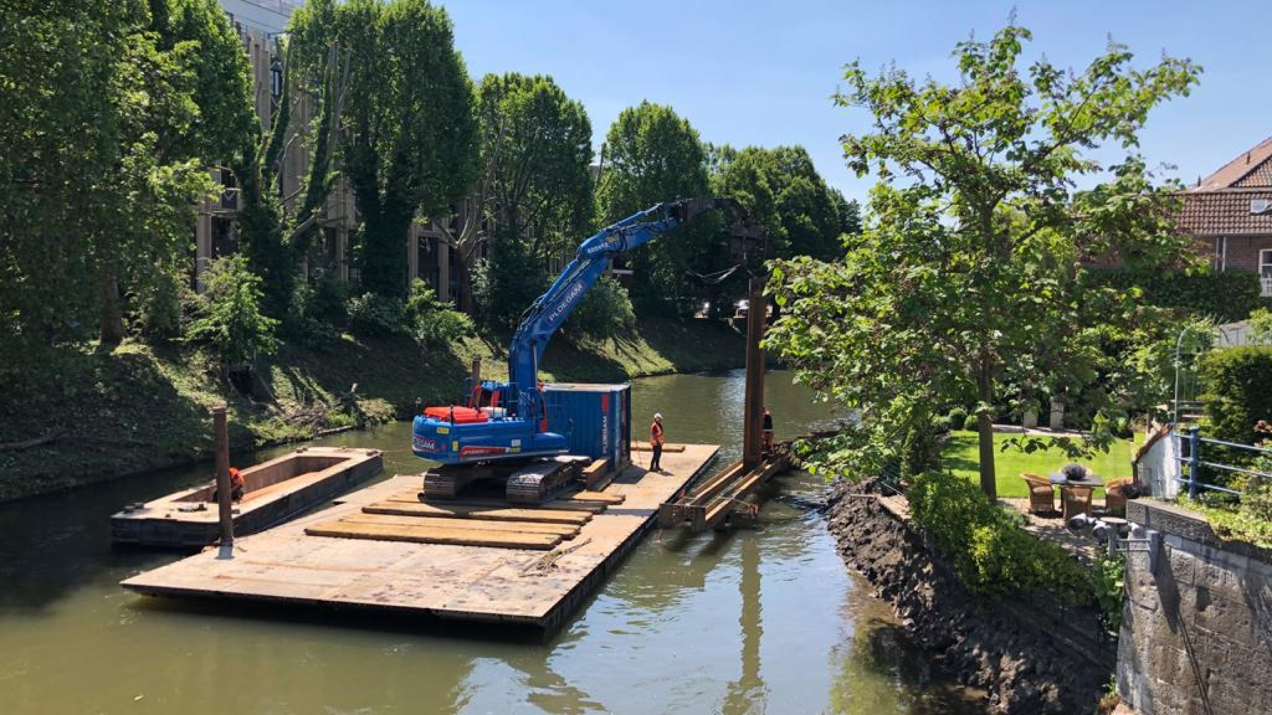 Blauwe Ploegam kraan plaatst damwanden vanaf een ponton