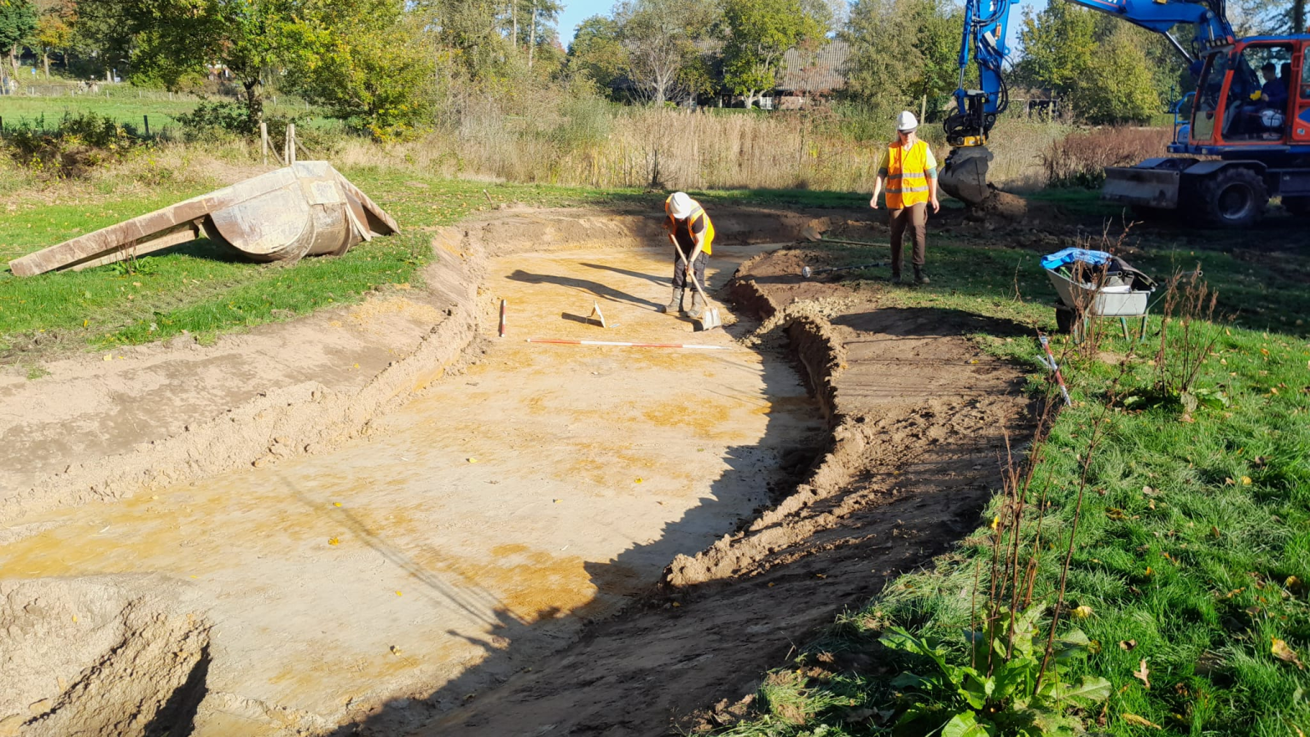 Bouwvakkers met witte helmen en veiligheidshesjes aan het werk met grondwerkzaamheden
