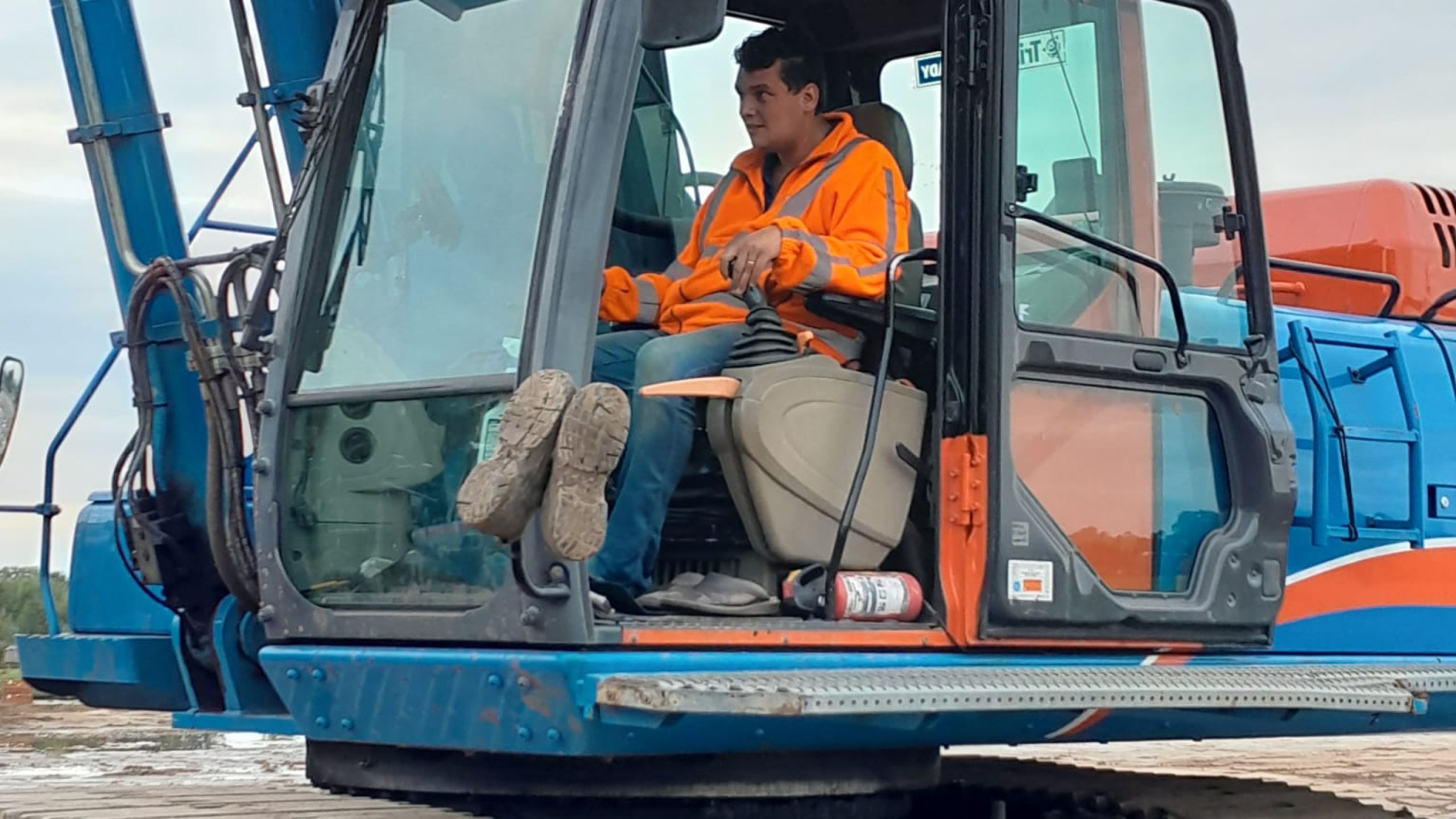 Man met oranje veiligheidsjas zit in de cabine van een blauwe kraan