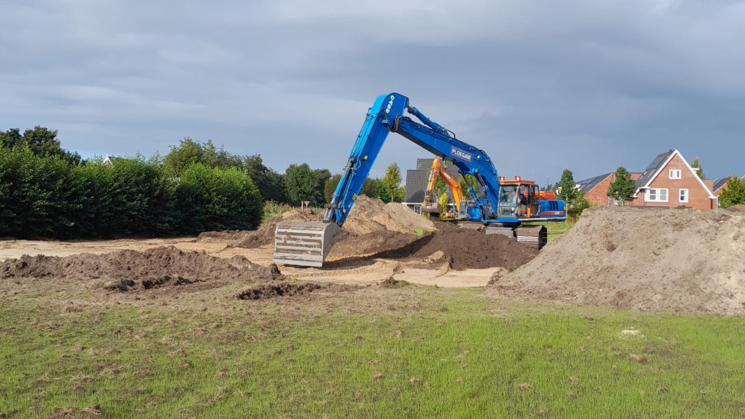 Blauwe Ploegam kraan tussen hopen zand met huizen op de achtergrond