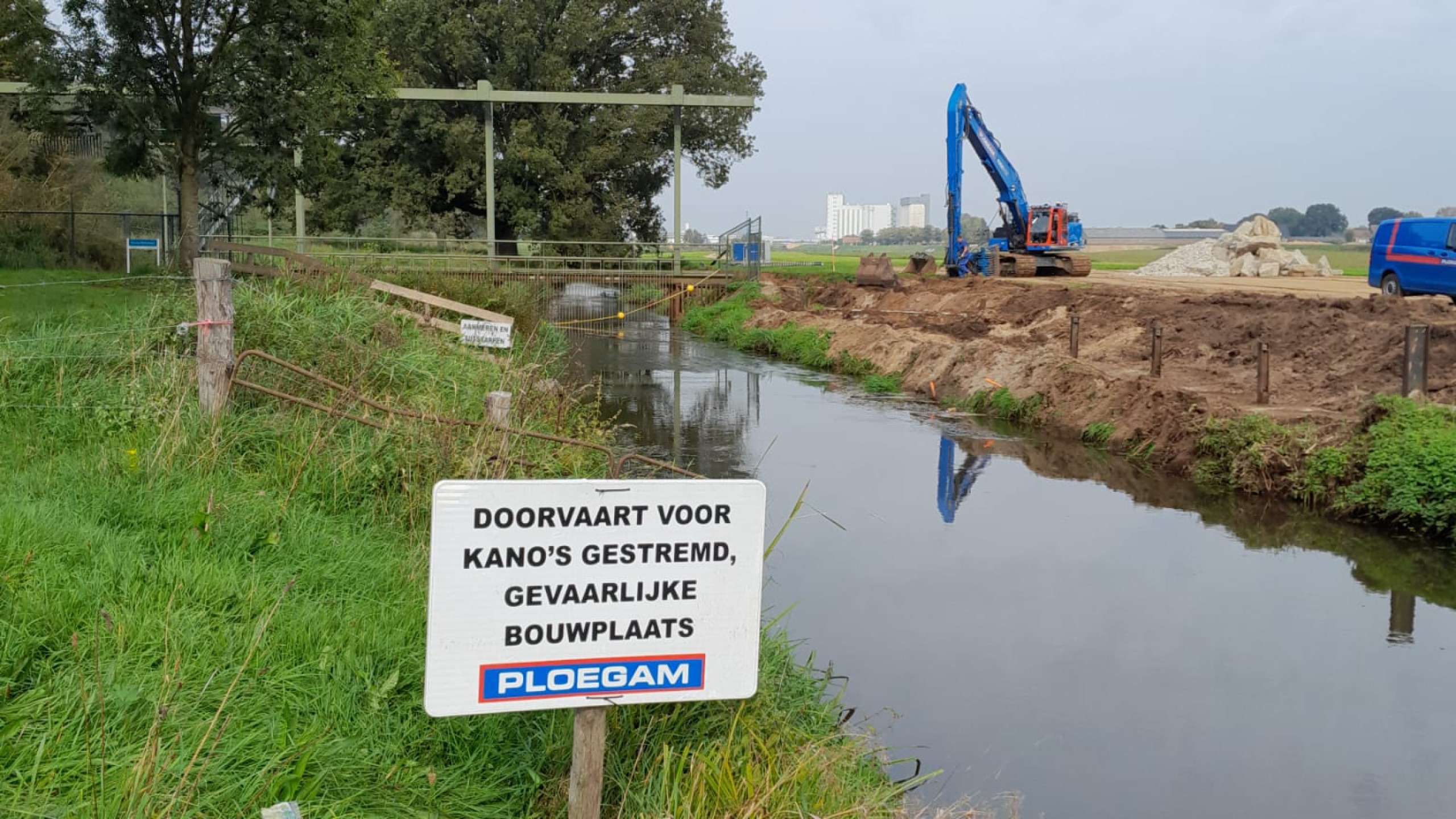 Blauwe Ploegam kraan naast een beek met bord over gestremde doorvaart voor kano's