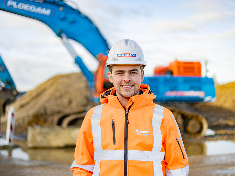 Medewerker Ploegam met oranje jas en helm met een blauwe kraan op de achtergrond