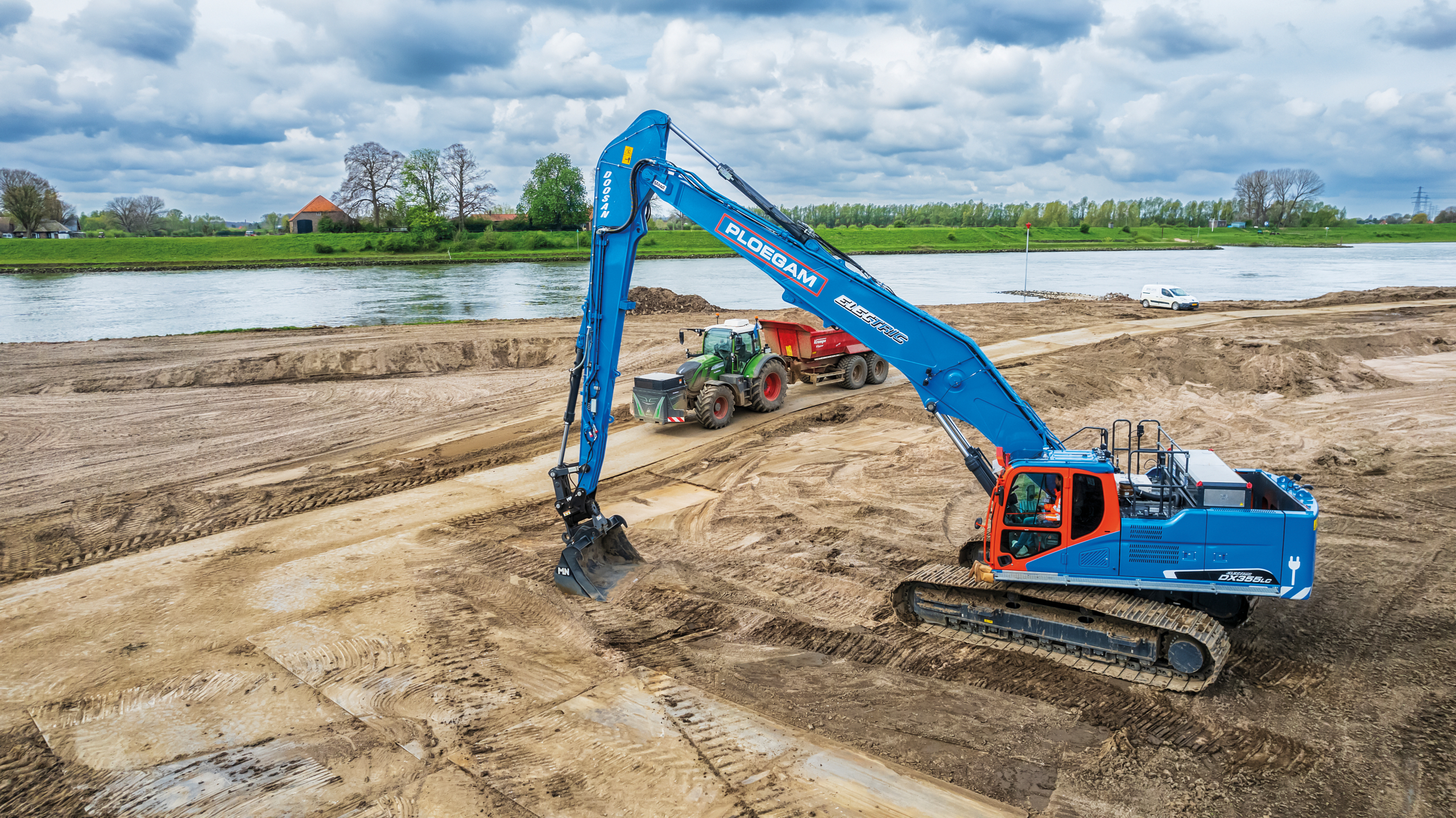 Elektrische Ploegam kraan met lange giek met tractor op het zand naast een rivier