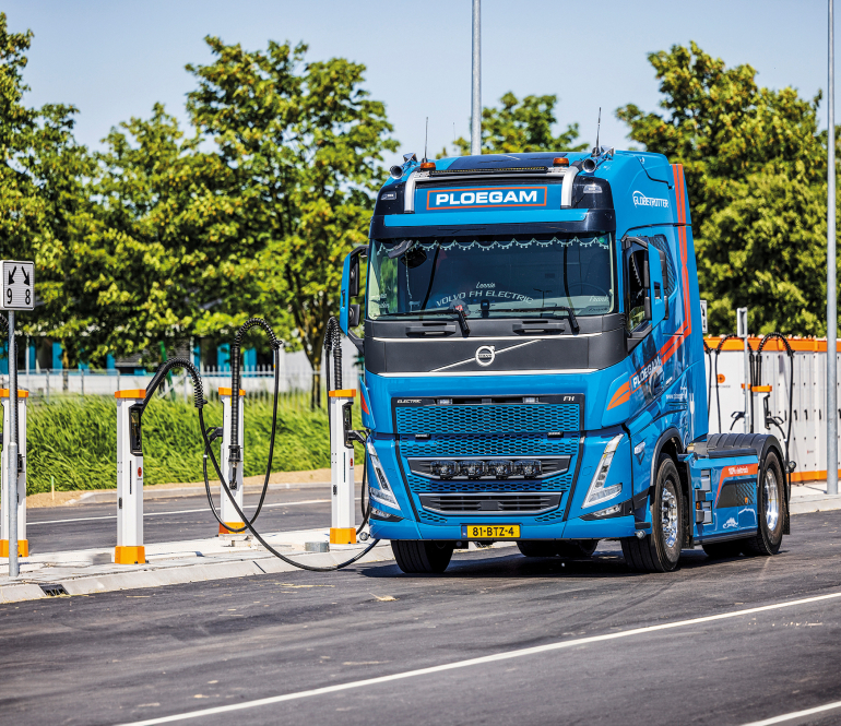 Blauwe Ploegam vrachtwagen aan laadpaal op laadplein voor elektrische vrachtwagens