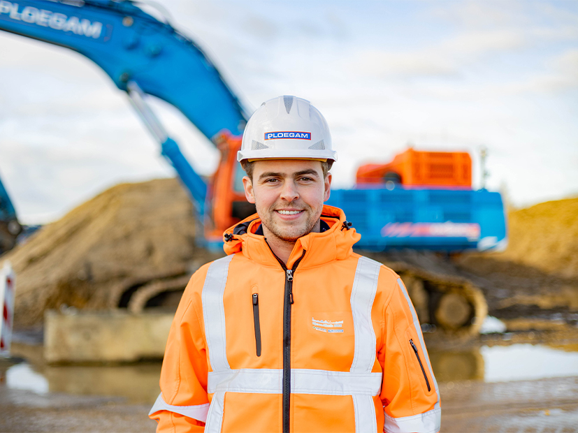 Man met oranje jas en witte helm met een blauwe kraan op de achtergrond