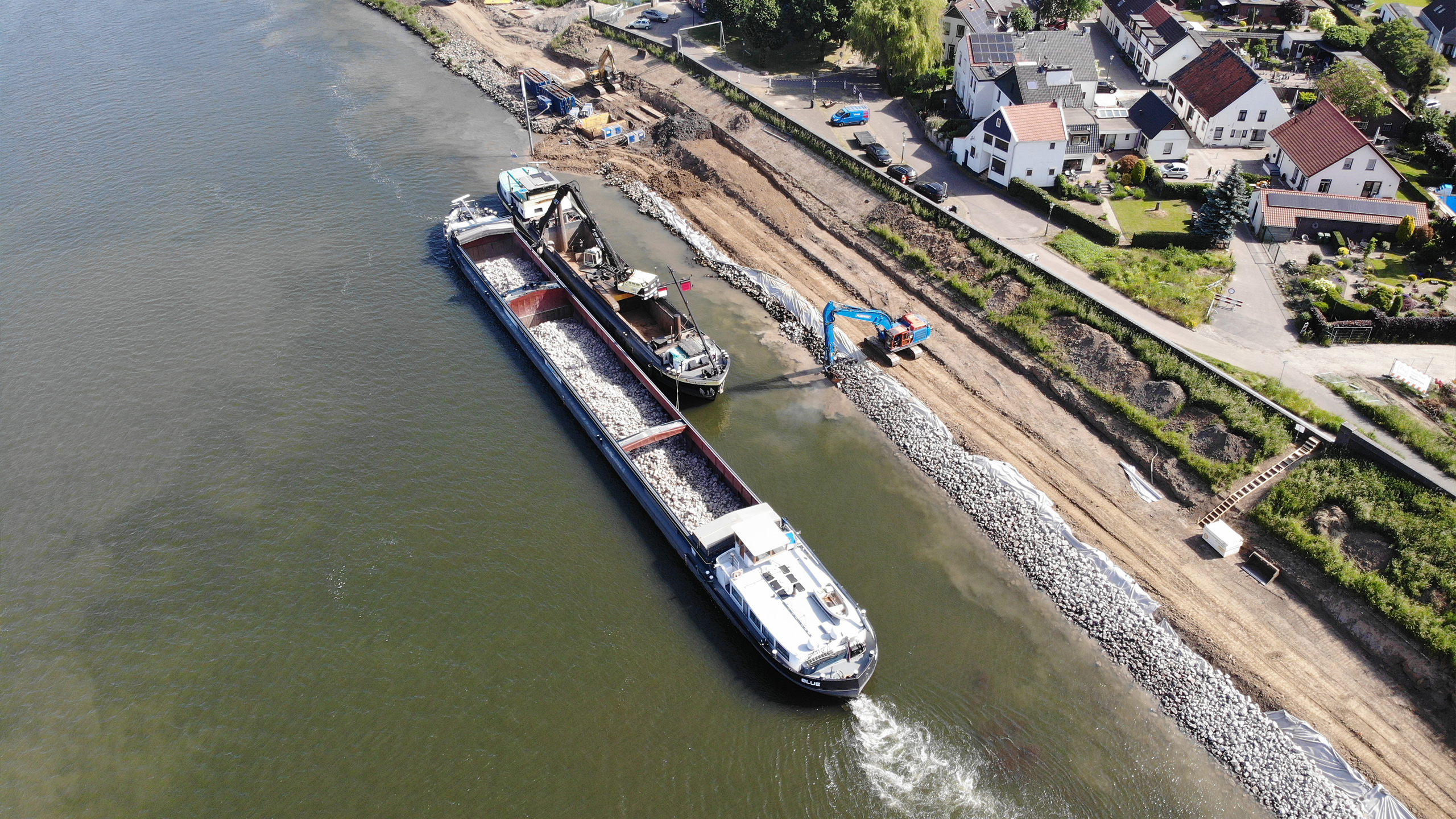Twee schepen op een rivier met een blauwe kraan en huizen op de achtergrond