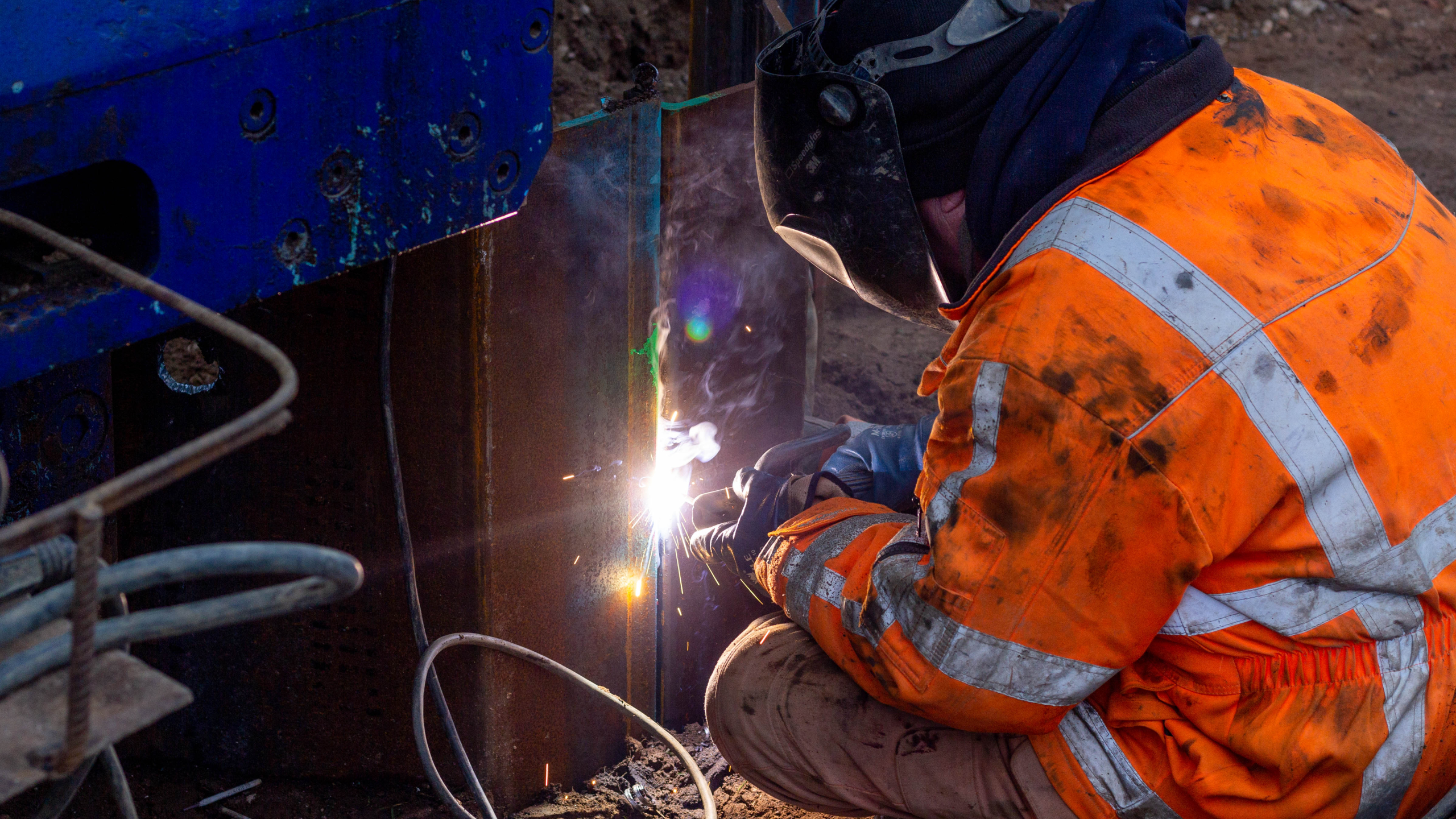 Man met oranje jas is een damwand aan het lassen met een lasapparaat