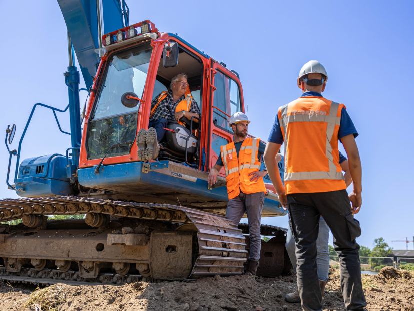Mannen met oranje veiligheidshesjes in het zand bij kraan