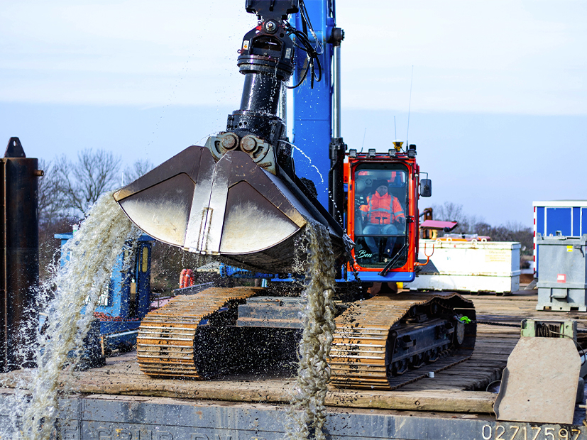 Man in blauwe Ploegam kraan aan het baggeren bij het water