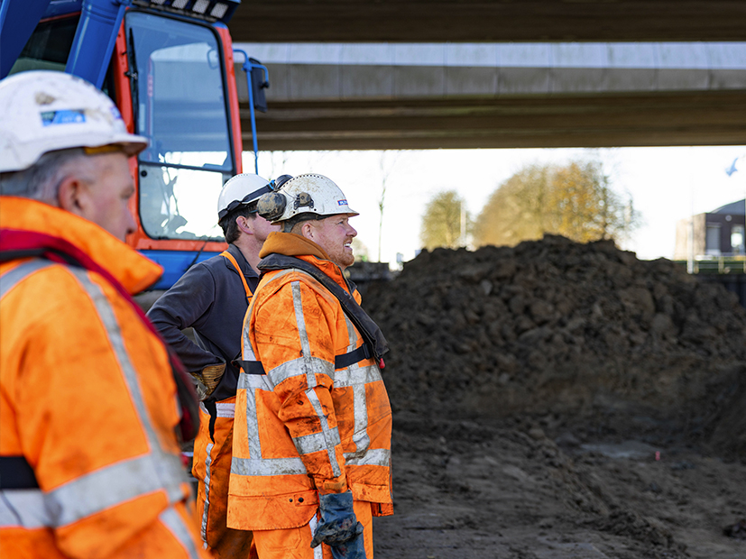 Mannen met oranje jassen en witte helmen met zand en kraan op de achtergrond