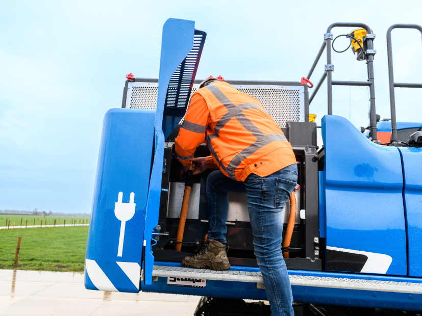 Man met oranje veiligheidsjas bij blauwe elektrische kraan