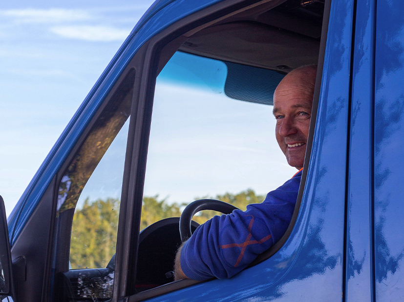 Man met blauwe trui kijkt uit het raam van een blauwe bus
