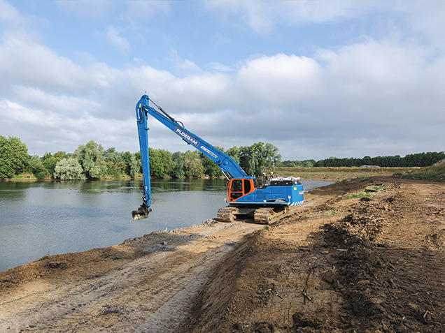 Blauwe elektrische kraan met lange giek op het zand naast een rivier