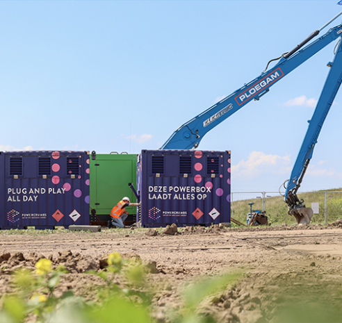 Man met veiligheidshesje bij accuboxen met de giek van een blauwe kraan op de achtergrond