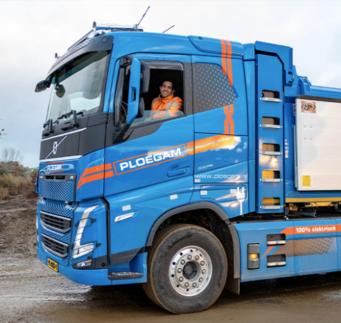 Lachende man kijkt door het raam van een blauwe Ploegam vrachtwagen
