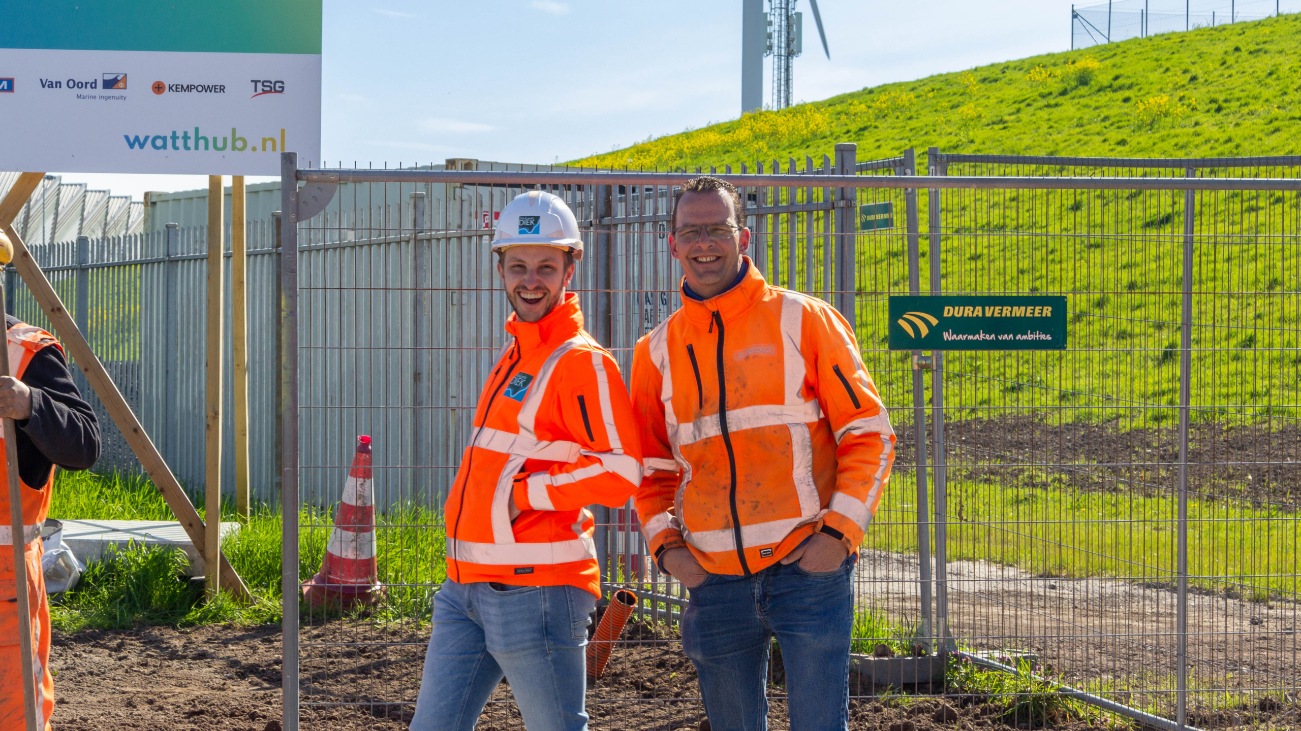 Twee lachende mannen in oranje veiligheidsjassen voor bouwhekken