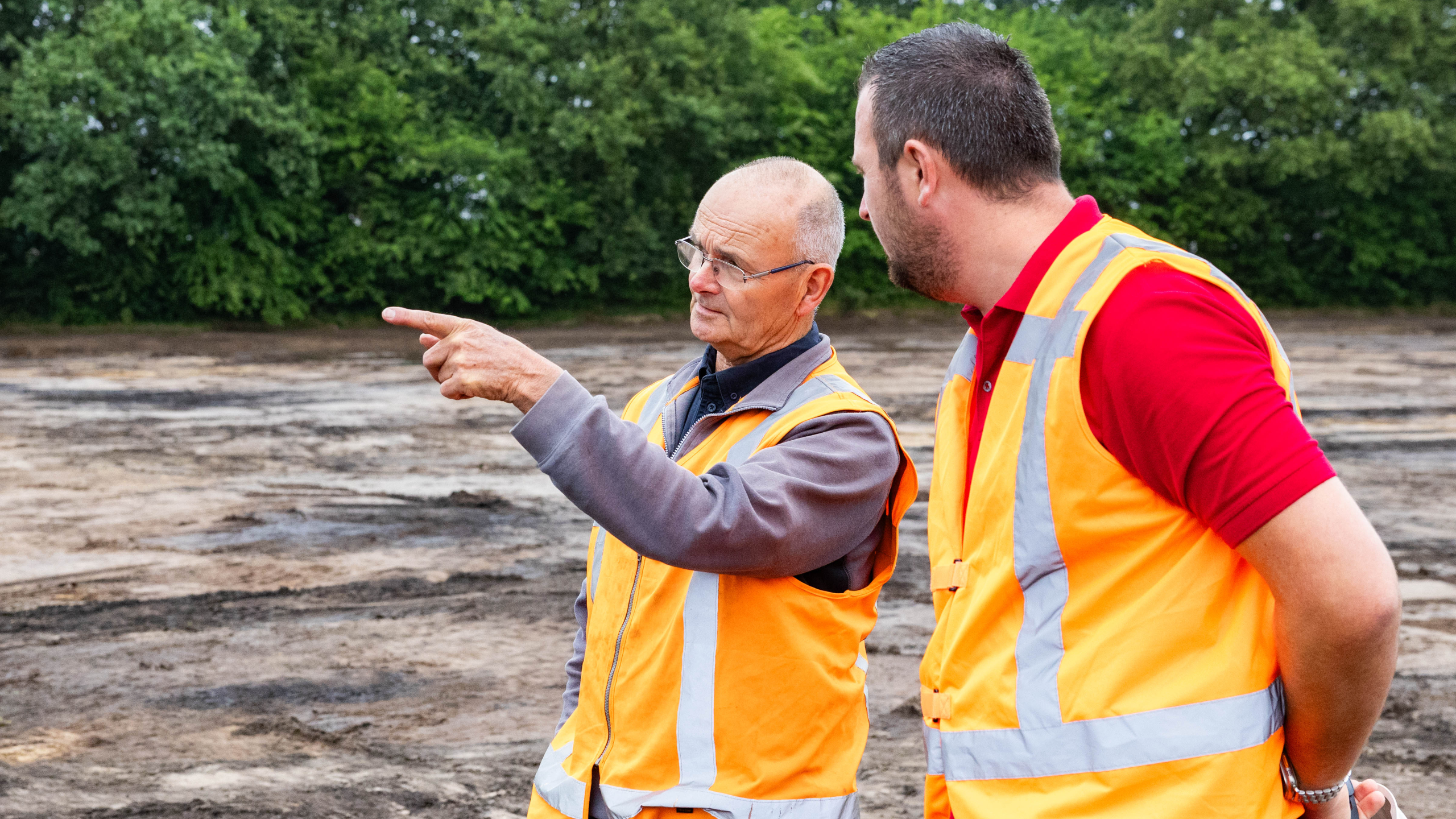 Twee mannen met oranje veiligheidshesjes in overleg op het zand