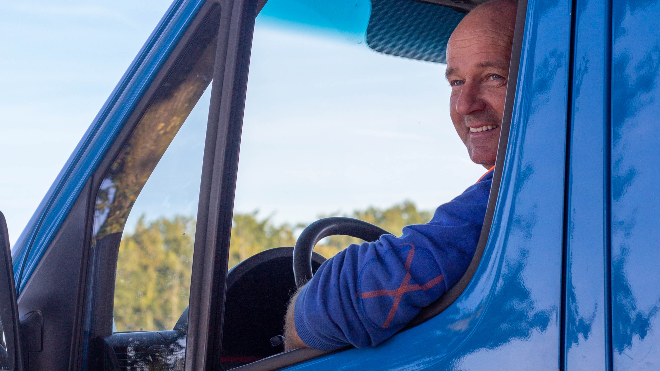 Lachende man kijkt naar buiten door het raam van een blauwe bus