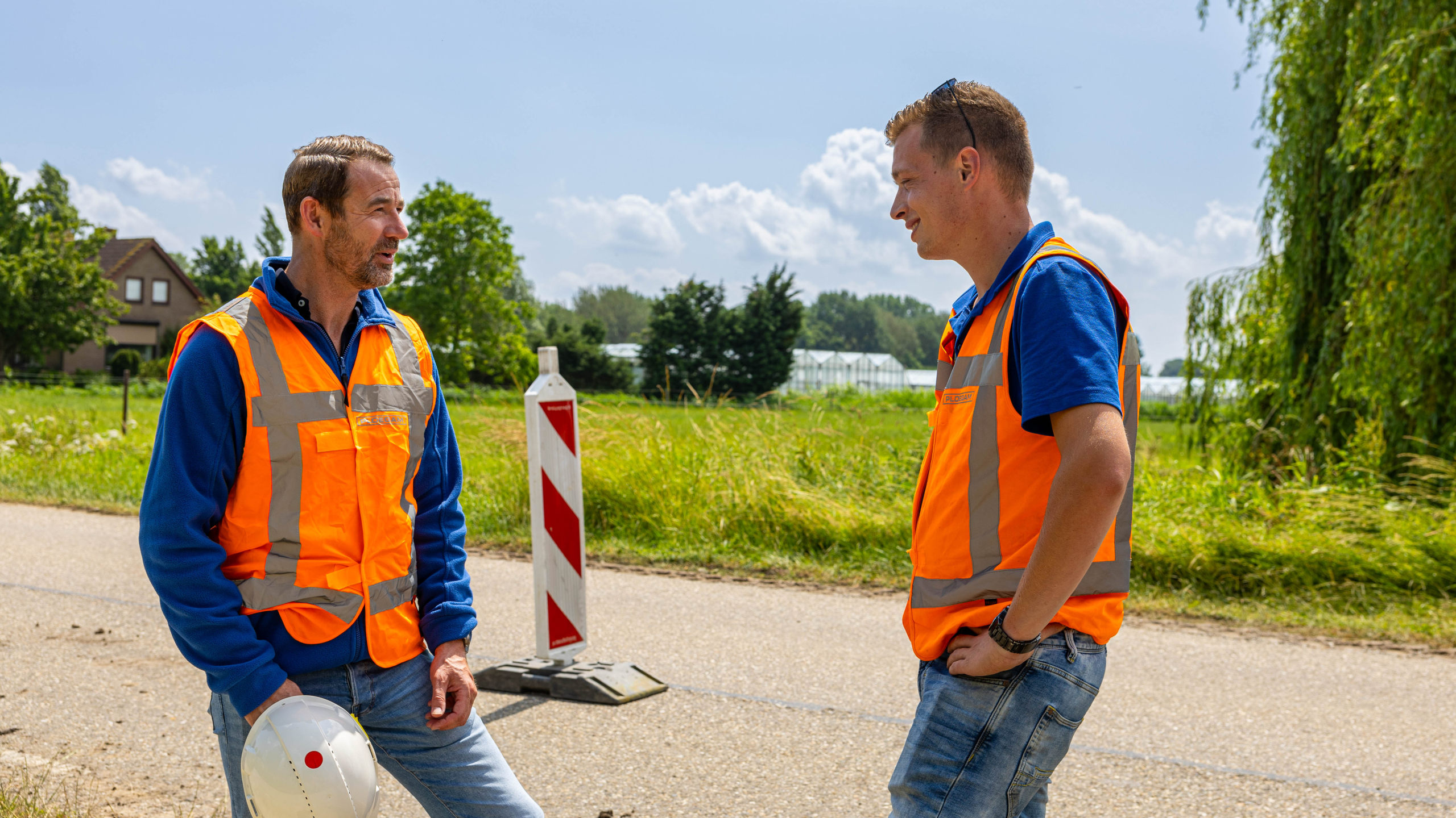 Twee mannen met oranje veiligheidshesjes in overleg op straat
