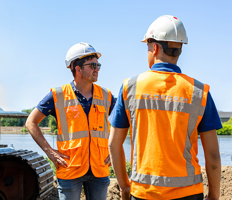 Medewerkers Ploegam met helm en oranje hesje op bouwplaats langs een rivier