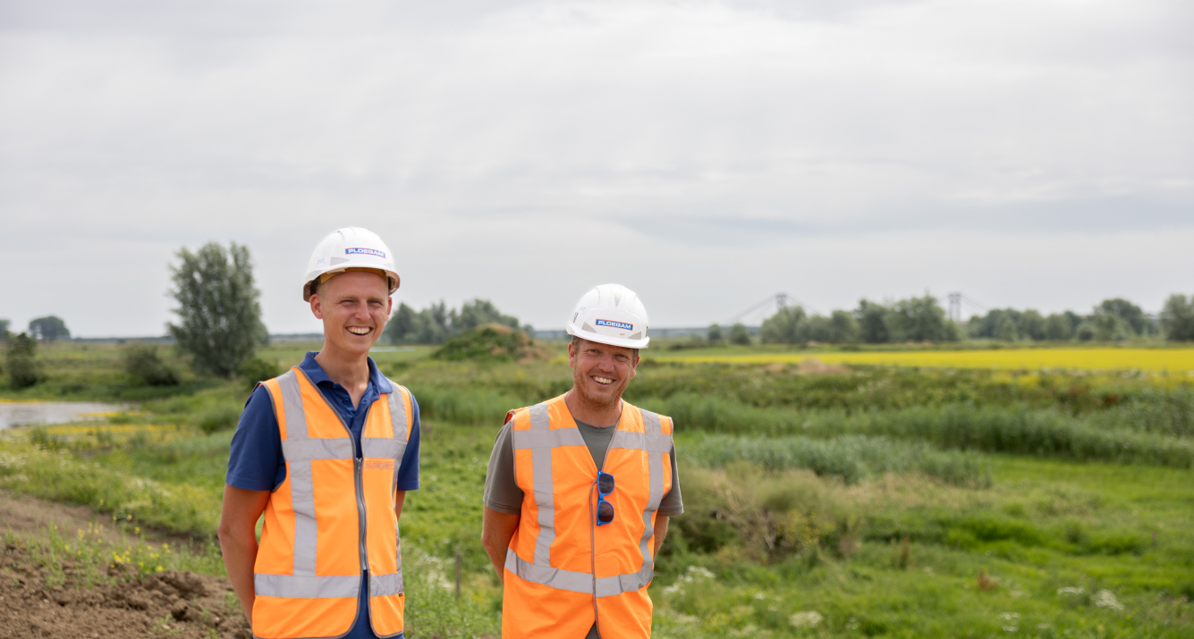 Man met oranje jas en witte Ploegam helm met een blauwe kraan op de achtergrond