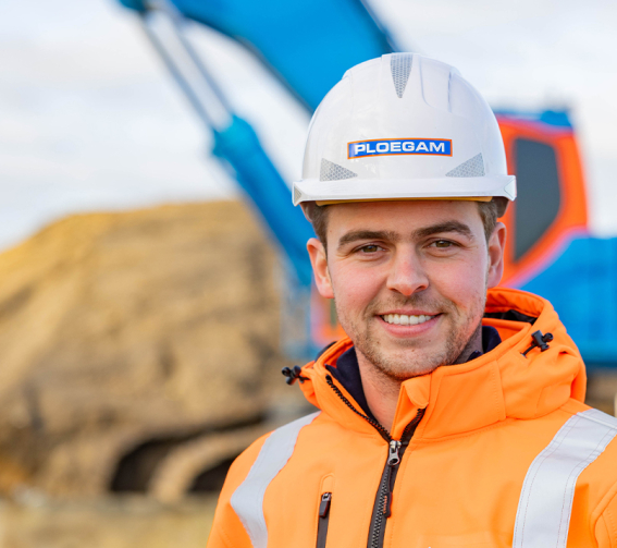 Man met oranje jas en witte Ploegam helm met een blauwe kraan op de achtergrond