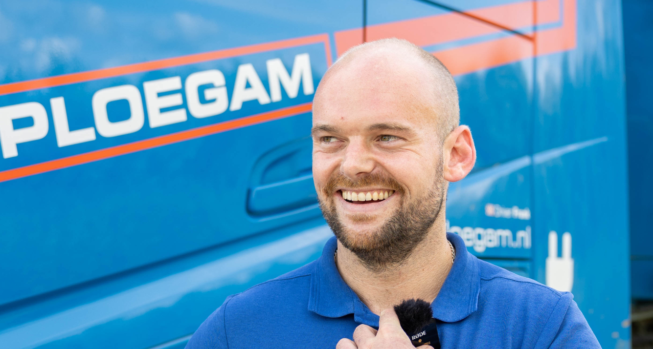 Man met oranje jas en witte Ploegam helm met een blauwe kraan op de achtergrond