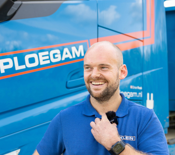 Man met oranje jas en witte Ploegam helm met een blauwe kraan op de achtergrond