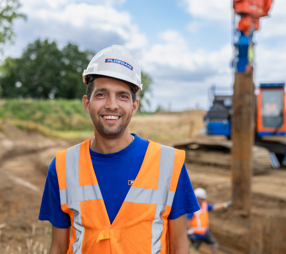 Man met witte Ploegam helm en veiligheidsjas met een blauwe Ploegam kraan op de achtergrond