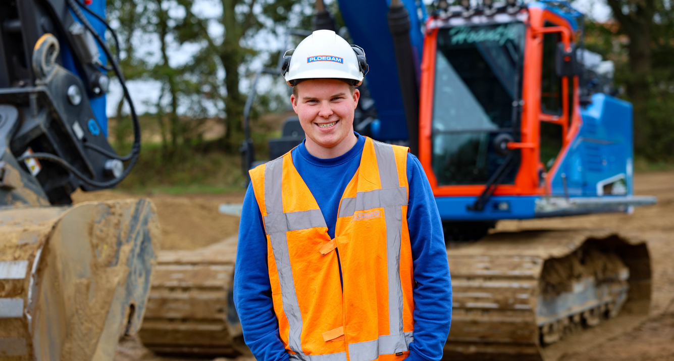 Man met oranje jas en witte Ploegam helm met een blauwe kraan op de achtergrond