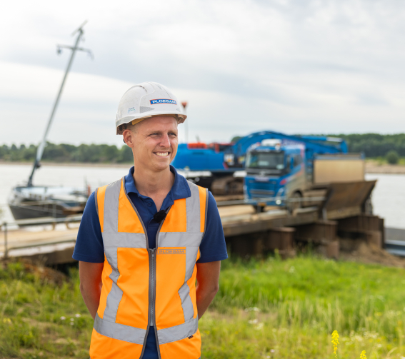 Man met oranje jas en witte Ploegam helm met een blauwe kraan op de achtergrond