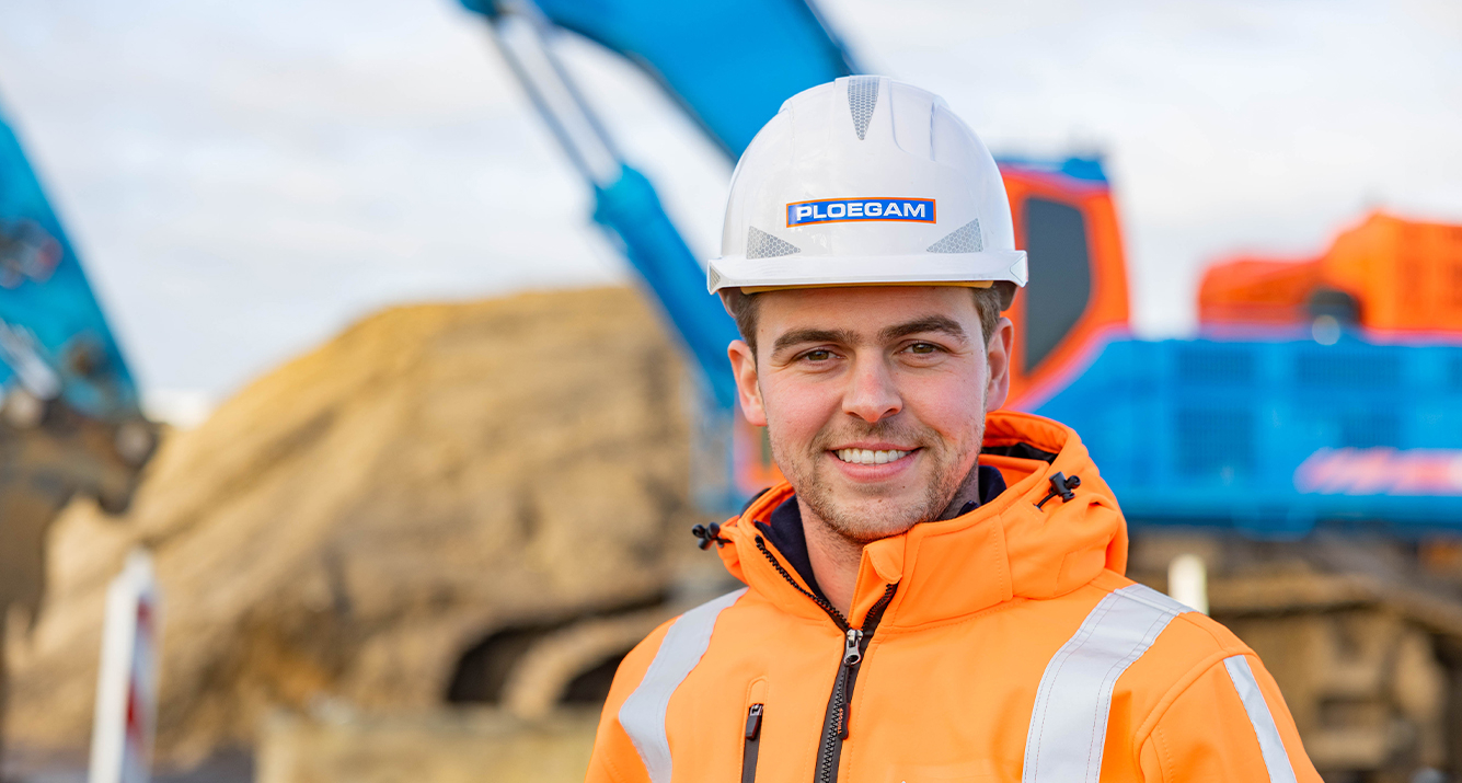 Man met oranje jas en witte Ploegam helm met een blauwe kraan op de achtergrond