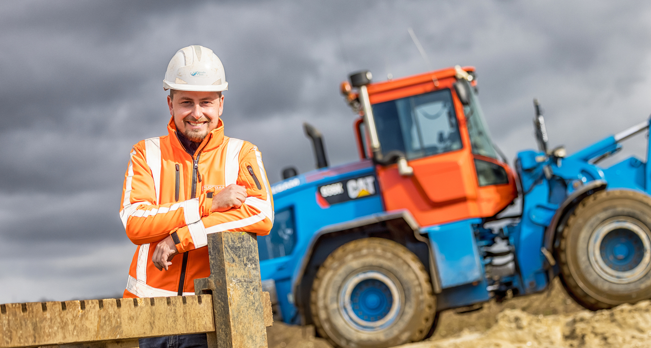 Man met veiligheidsjas en helm op bouwplaats met blauwe shovel op de achtergrond